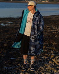 **MALE** Man stood on a beach wearing a cap and dryrobe Advance Long Sleeve changing robe in Blue Camo Blue