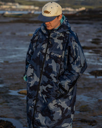 **MALE** Man stood on a beach wearing a dryrobe Advance Long Sleeve changing robe in Blue Camo Blue