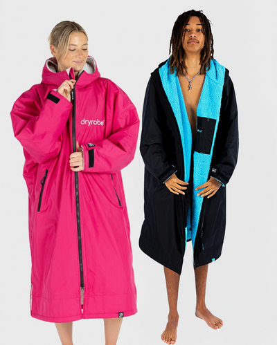 Two people wearing dryrobes, one pink and one black with blue lining, on a white background.
