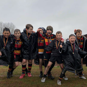 Group of young boys in sports uniforms and dryrobes posing together outdoors.