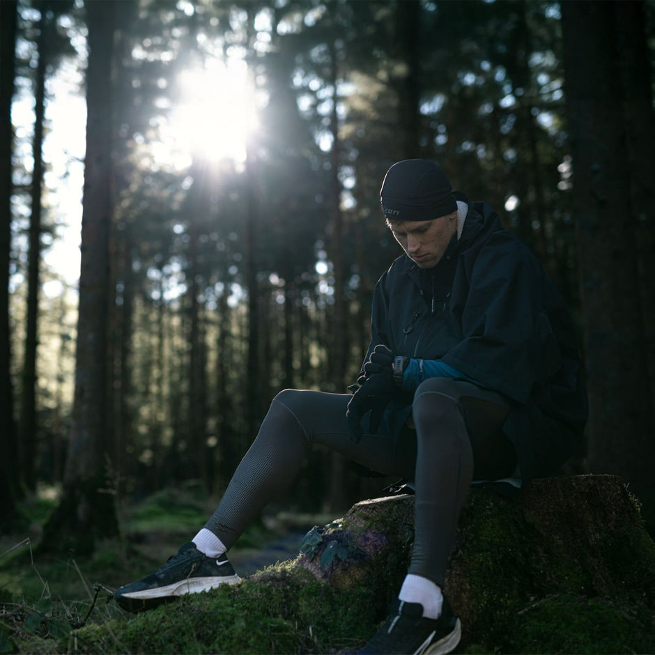 Person sitting on a log wearing a Dryrobe® Lite Jacket in a forest with sunlight filtering through the trees