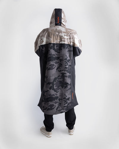 *MALE* A hooded Dryrobe Nexus shown from the back on a model, featuring a two-tone design with a beige and grey camouflage pattern on the upper portion and a dark grey and black camouflage pattern on the lower portion. The brand name 'dryrobe' is visible in orange on the hood and lower side.