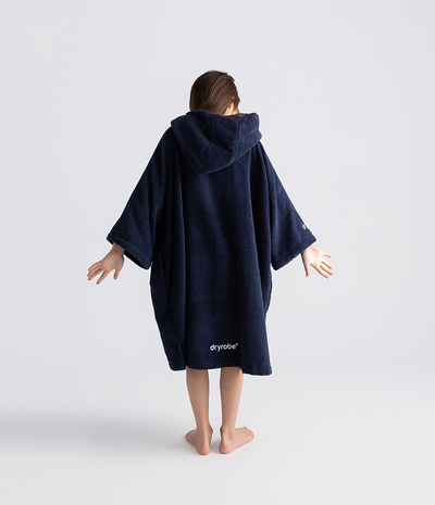 Person wearing a navy blue hooded towel robe with 'dryrobe' branding on a white background