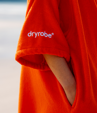 Person wearing a orange dryrobe with 'dryrobe' branding on a blurred beach background