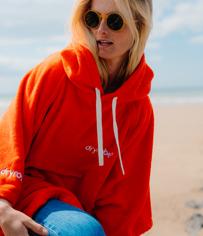 Person wearing a orange hooded towel robe with 'dryrobe' branding on a beach.
