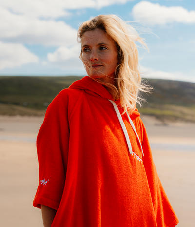 Woman wearing a orange hooded towel robe with a logo on a beach