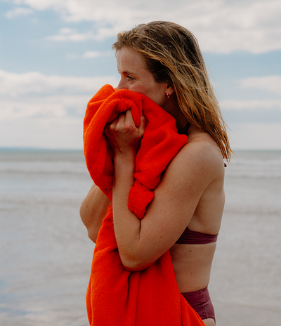 Woman wrapped in an orange towel robe on a beach with a cloudy sky.
