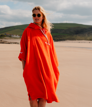 Person wearing a bright orange hooded towel robe on a beach with green hills in the background