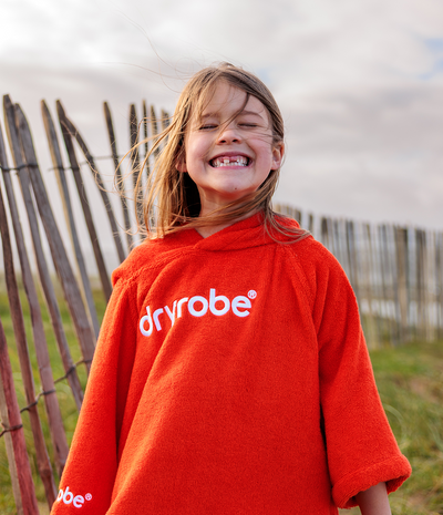 Person wearing a red 'dryrobe' towel robe outdoors with a wooden fence and sky in the background
