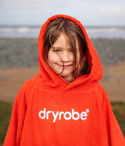 Child wearing a red dryrobe towel robe outdoors with a blurred natural background