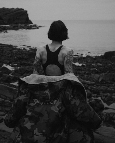 Person with tattoos sitting on rocks by the ocean