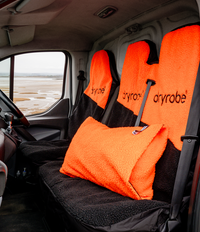 Orange and black Dryrobe® seat covers and an orange and black cushion cover in a vehicle with a beach in the background