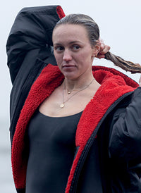 Young woman wearing Black Red dryrobe® Advance on the beach