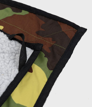 Close-up of a quilted patch with a green, brown, and black camouflage pattern, a black woven border, and a white sherpa lining.