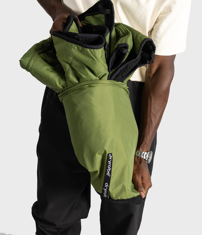 A person holding an olive green dryrobe picnic blanket jacket with black fleece lining, showing the brand 'dryrobe' on a black label sewn on.