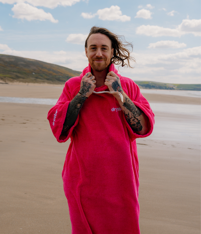 *MALE* Person wearing a bright pink towel robe on a beach with a scenic background