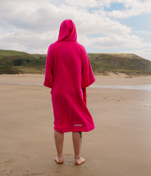 *MALE* Person wearing a pink hooded towel on a beach with a scenic background
