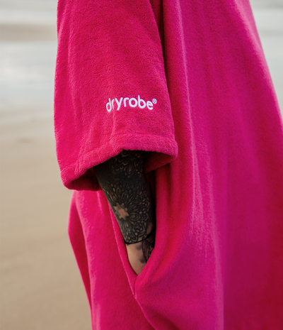 *MALE* Pink robe with 'dryrobe' logo worn by a person on a beach.