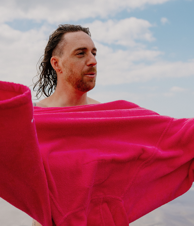 *MALE* Man with a pink towel robe draped over his shoulders against a cloudy sky.