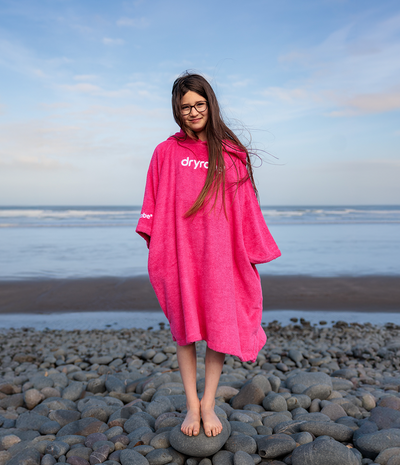 Person wearing a pink 'dryrobe' towel robe on a beach