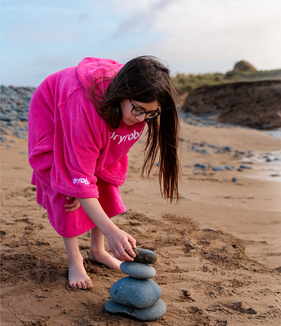Person in a pink towel robe stacking stones on a beach