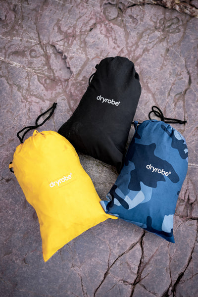 Three drawstring bags in yellow, black, and blue camouflage on a textured stone surface with 'dryrobe' branding.