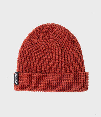 A rust red ribbed knit beanie hat with a folded cuff, featuring a small black 'dryrobe' brand tag on the side, set against a plain light gray background.