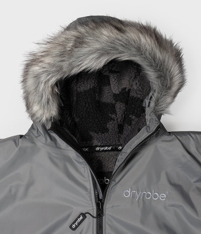 *MALE* Close-up of a gray Dryrobe hooded jacket with a fluffy gray faux-fur trim around the hood and a black fleece-lined interior. The Dryrobe logo is visible on the chest and zipper pull.