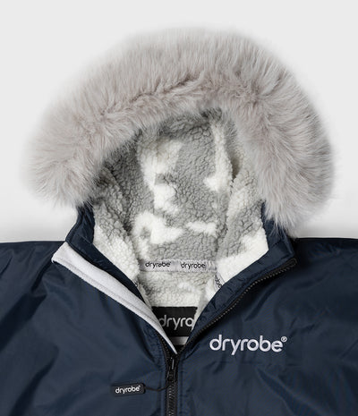 *MALE* Close-up of a navy blue Dryrobe hooded jacket with a fluffy light gray faux-fur trim and a white sherpa lining, showing the Dryrobe brand on the chest and collar.