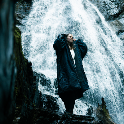 Person standing in front of a waterfall wearing a dark coat.