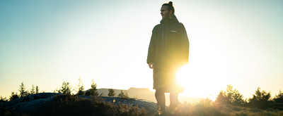 Person standing on a hill with the sun setting behind them, creating a silhouette effect.