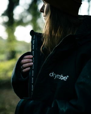 Person wearing a black jacket with 'dryrobe' branding, standing outdoors.