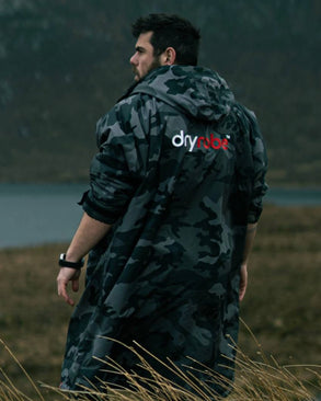 Person wearing a camouflage dryrobe with 'dryrobe' logo in a natural setting