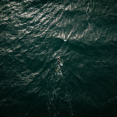 A person swimming through dark blue ocean waves from an aerial perspective.