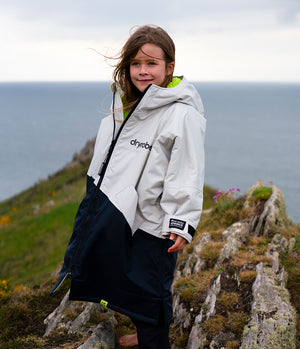 Child wearing a white jacket with 'dryrobe' branding on a cliffside with ocean view