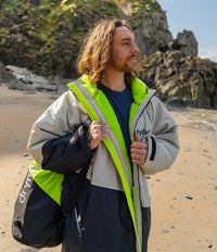 *MALE* Man standing on a beach wearing a Dryrobe with a visible brand logo, holding a bag.