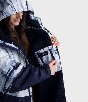 Person wearing a patterned Dryrobe with a hood, holding the Dryrobe open to reveal a brand logo.