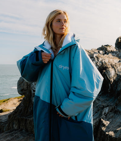Person wearing a blue and white Dryrobe with 'dryrobe' branding by the ocean.