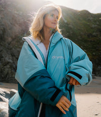Person wearing a blue and teal dryrobe on a beach with mountains in the background