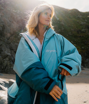 Person wearing a blue and teal dryrobe on a beach with mountains in the background