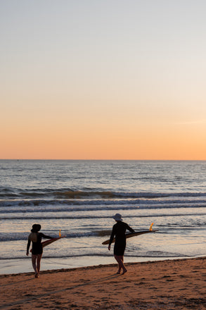 Two people walking on a beach at sunset with a calm ocean.