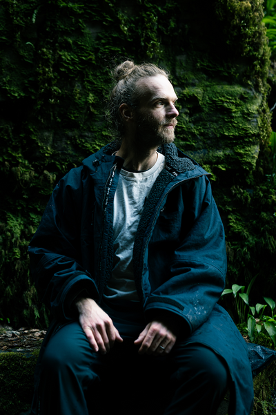 Person in a blue robe sitting against a moss-covered stone wall