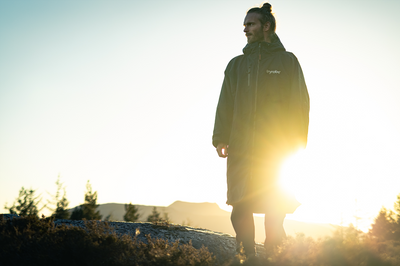 Person wearing a raincoat standing in a field with a sunset or sunrise in the background