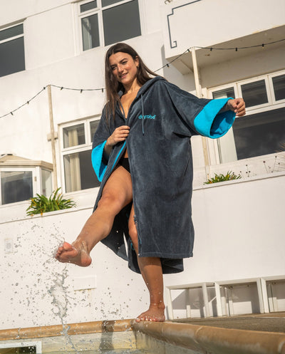 Woman wearing a dark grey and blue towel robe by a poolside with a building in the background