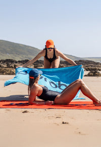 Two people laying Dryrobe® towel robes on the beach 