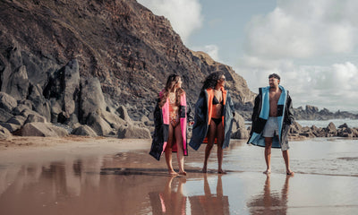 Three people walking on a beach with rocky cliffs in the background