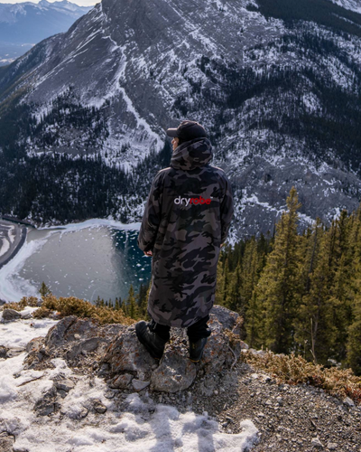 Person standing on a mountain top with a scenic view of a lake and mountains.