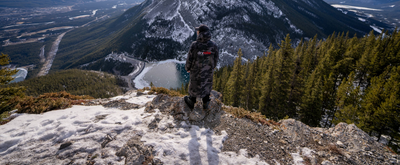 Person standing on a mountain top with a scenic view of a lake and mountains.