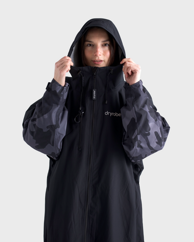 Person wearing a black and camouflage raincoat with 'Dryrobe' branding on a white background