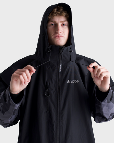 *MALE* Person wearing a black hooded jacket with 'dryrobe' branding on a light grey background